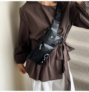Detail of street style black pebbled leather chest bag with multi-zipper layers and buckles