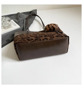 Detail view of leopard print faux fur tote bag with smooth leather base and plush pendant