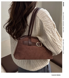 Close-up of brown suede tote bag featuring smooth leather straps and gold buckle detail