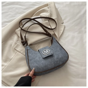 Detail of the gray hobo bag featuring a metal M logo buckle and brown leather trim