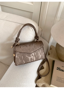 Detailed view of brown textured leather bag with gold artistic splash and knotted handle