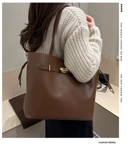 Close-up of brown leather tote bag showing golden buckle and side drawstring details