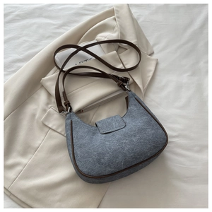 Detail of grey felt crescent bag with brown leather trim on a white blazer background
