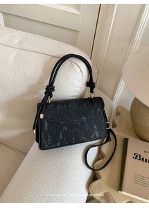 Detail of black marble textured small square bag on a soft sofa with golden hardware