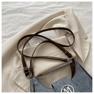 Detail of blue denim fabric texture and silver M logo on a crescent shoulder bag