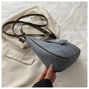 Close-up of saddle-shaped denim shoulder bag with brown leather trim and metal logo