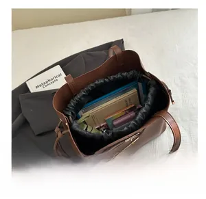 Detail view of brown leather tote bag showing large capacity and drawstring inner pouch