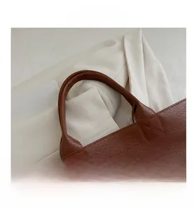 Detailed macro view of brown lychee grain leather texture and handle strap on the tote bag