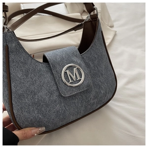 Detail of grey denim hobo bag featuring brown leather trim and silver metal M logo buckle
