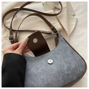 Close-up of crescent shoulder bag magnetic buckle and textured fabric with leather trim