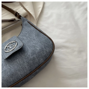 Detail of blue textured fabric with brown leather trim and silver M-logo buckle