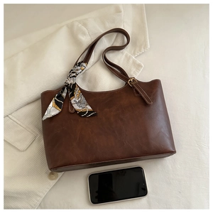 Détail du sac cabas vintage marron avec foulard en soie à motifs sur fond texturé blanc