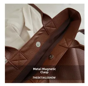 Detailed view of the magnetic metal clasp on a textured brown leather tote bag