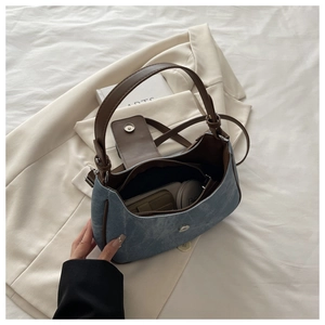 Detail of the blue denim underarm bag with brown leather trim and magnetic buckle