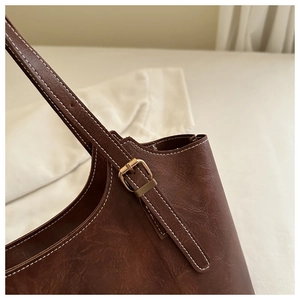 Gros plan détaillé du sac cabas en cuir marron foncé avec surpiqûres blanches et boucle dorée
