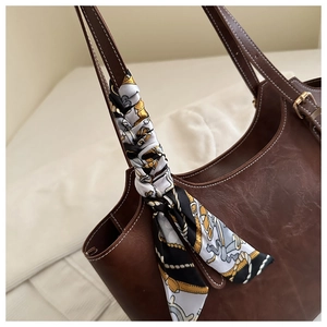 Gros plan d'une anse de cabas en cuir marron avec un foulard en soie et des surpiqûres claires