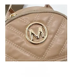 Detail shot of quilted latte leather bag with round gold metal M logo and zipper