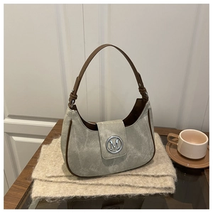 Close-up of a grey-green suede Hobo bag with brown leather edges and silver M logo
