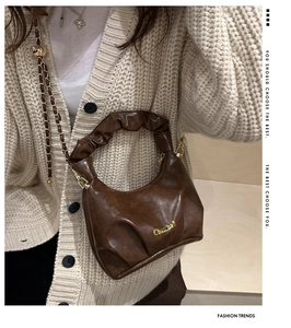 Detail of a brown leather crossbody bag featuring a pleated handle and gold chain strap