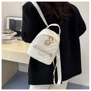 Close-up of white quilted mini backpack with gold M logo on a model in a black blazer