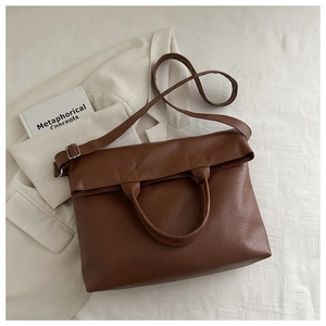 Top view of brown lychee grain leather tote bag with silver hardware on cream blazer