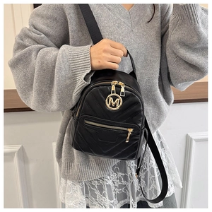 Detail of black mini leather backpack with V-quilted texture and golden M letter logo buckle