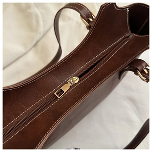 Détail du sac cabas en cuir marron avec fermeture éclair dorée et coutures blanches contrastées