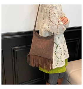 Sac bandoulière marron en daim avec franges porté sur un pull en maille blanc