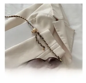 Detail view of dark brown ruched bag with gold chain strap on a white blazer