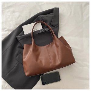 Detail of brown faux leather tote bag with vertical stitching on grey suit background