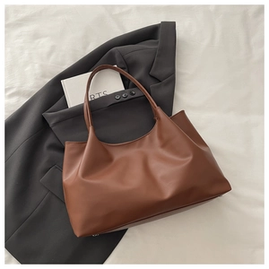 Detailed close-up of brown leather tote bag stitching and metal feet on grey blazer