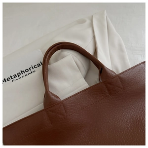 Detailed close-up of brown pebbled leather tote bag showing reinforced cross stitching