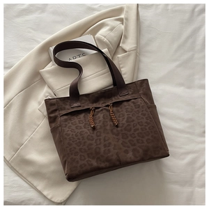 Detail of dark brown tote bag featuring subtle animal print texture and woven drawstring tassels
