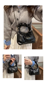 Detail of black pleated handle handbag with golden chain strap and logo lettering