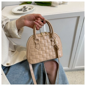 Detail of quilted apricot shell bag with gold hardware held by model in white suit