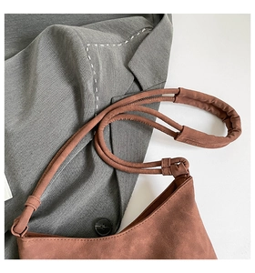 Close-up of brown suede shoulder bag with tassel details on a grey blazer