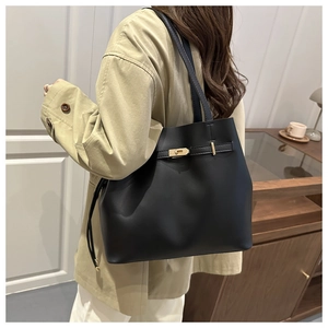Dettaglio di una grande borsa a secchiello in pelle nera con fibbia dorata sul trench