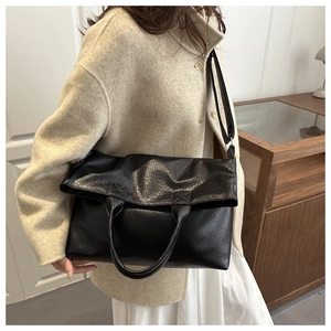 Detail of black lychee texture leather tote bag worn as a crossbody with wide strap