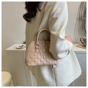 Detail der beigen Muscheltasche mit Schachbrettmuster, getragen zu einem weißen Blazer