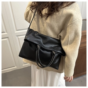 Detail of black pebbled leather tote bag with adjustable strap and minimalist fold closure