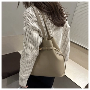 Detail of a beige leather bucket bag with gold clasp shown on a shoulder in lifestyle setting