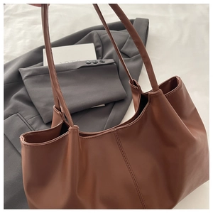 Detailed texture of brown leather tote bag draped on a grey blazer for daily commute
