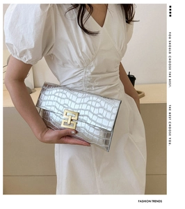 Detail of silver crocodile pattern envelope clutch with a gold buckle held by a model