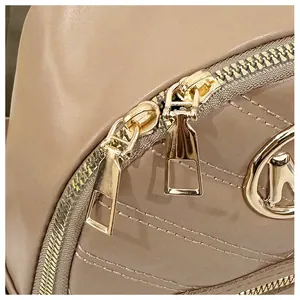 Detail of beige quilted leather bag with dual gold zippers and metallic logo accent