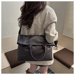 Detail of dark brown lychee leather texture and wide shoulder strap on a tote bag