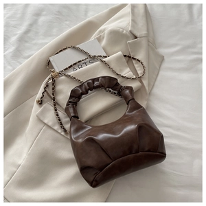 Detail of dark brown ruched crescent bag with glossy texture and gold chain strap