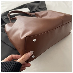 Detail shot of brown tote bag bottom showing silver metal protective feet and fine stitching