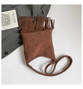 Detailed view of a brown suede handbag with long decorative tassels and a soft shoulder strap