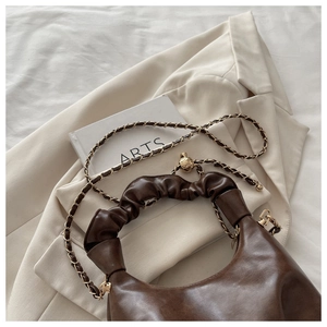Detail of dark brown glossy bag with gold chain strap and textured round metal hardware