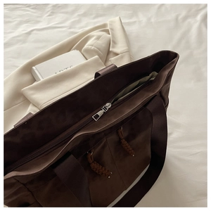 Detail of dark brown tote bag featuring top zipper closure and decorative woven drawstring